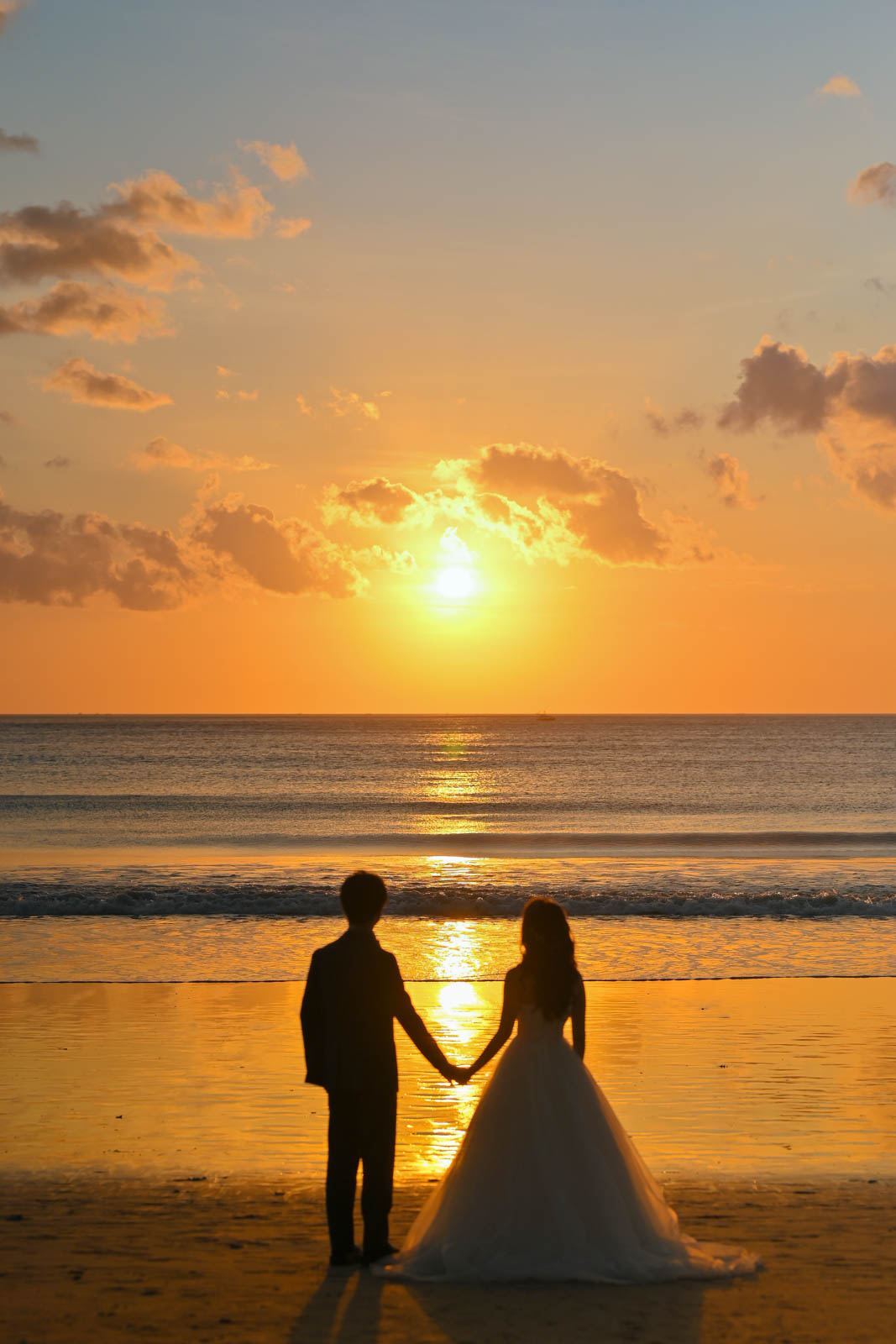 夕陽を眺めながら手を取り合う新郎新婦の後ろ姿｜ジンバランビーチ
