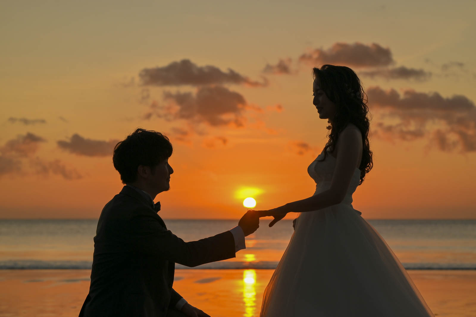夕日を背景に指輪を交わす新郎新婦のシルエット｜ジンバランビーチのフォトウェディング