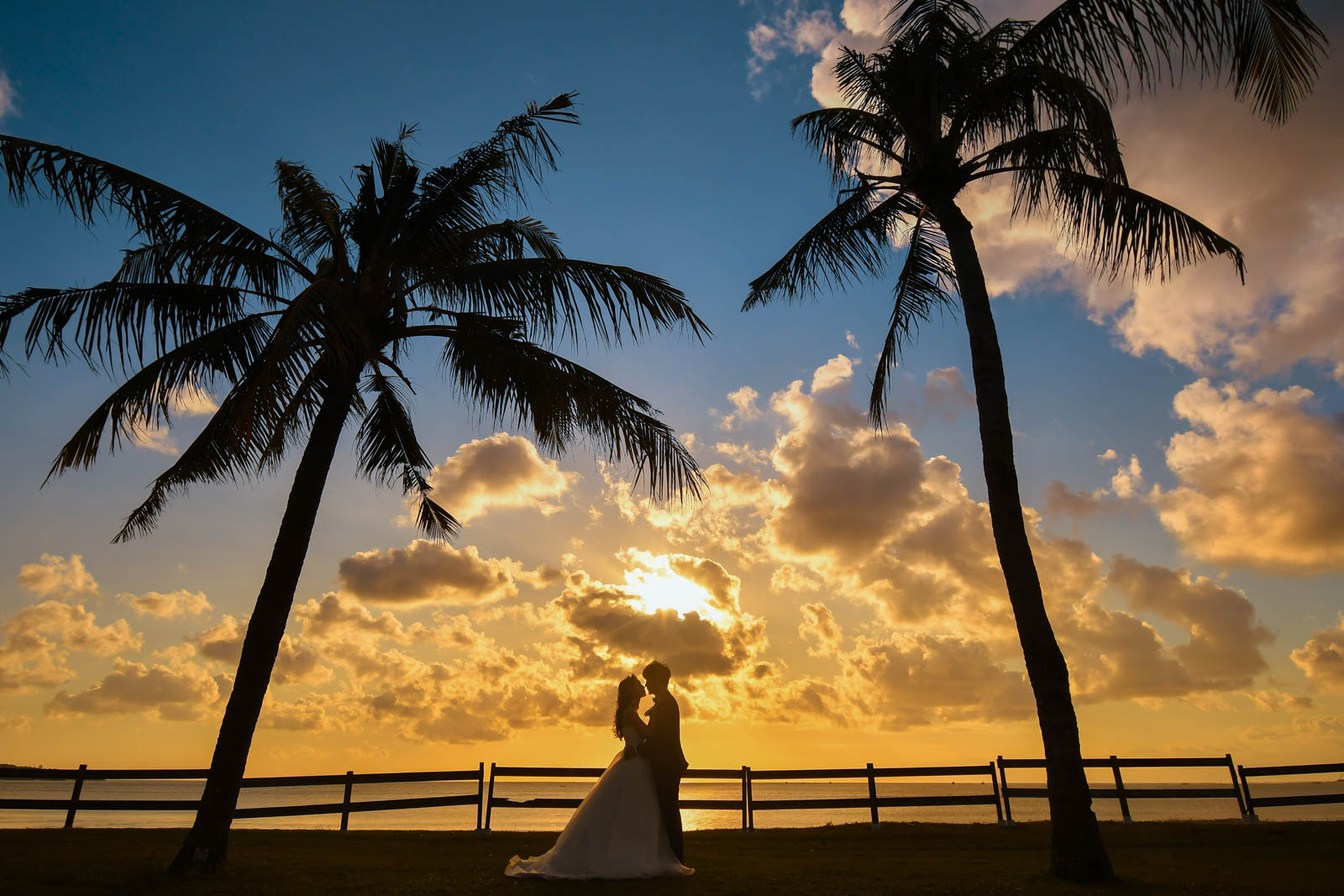 ヤシの木と夕日を背景にシルエットで見つめ合う新郎新婦｜ジンバランビーチのサンセットフォト