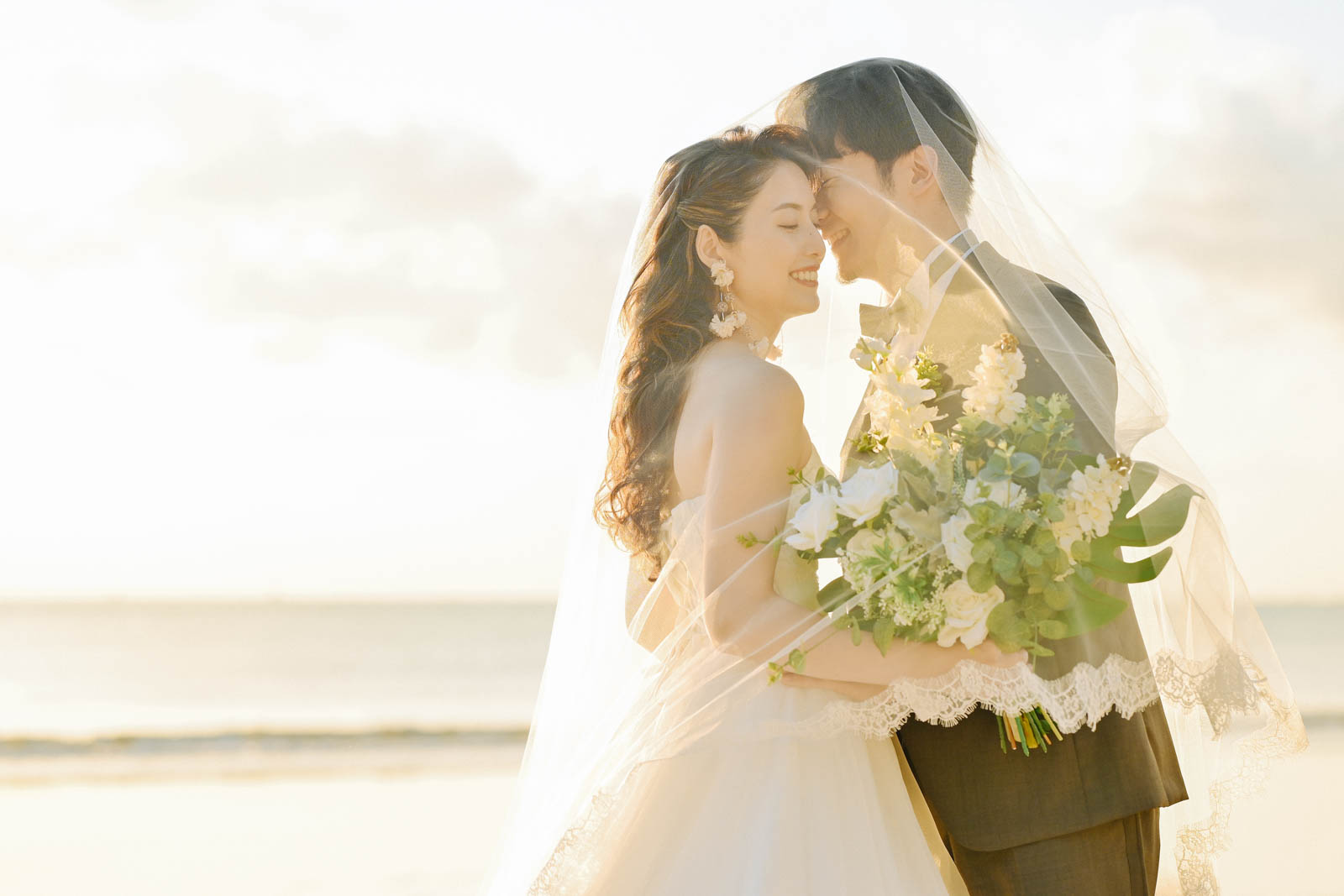 夕日に包まれたビーチでベール越しに微笑み合う新郎新婦｜ジンバランのフォトウェディング