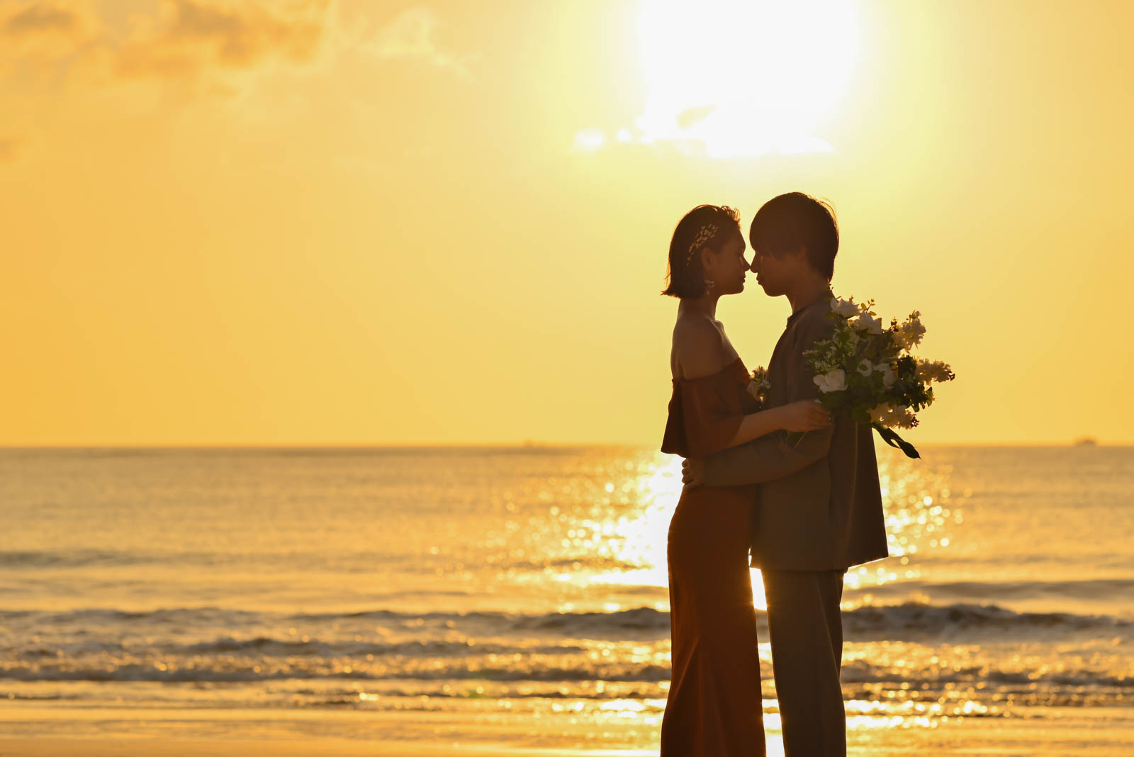 黄金色の光に包まれてキスをする新郎新婦のシルエット写真