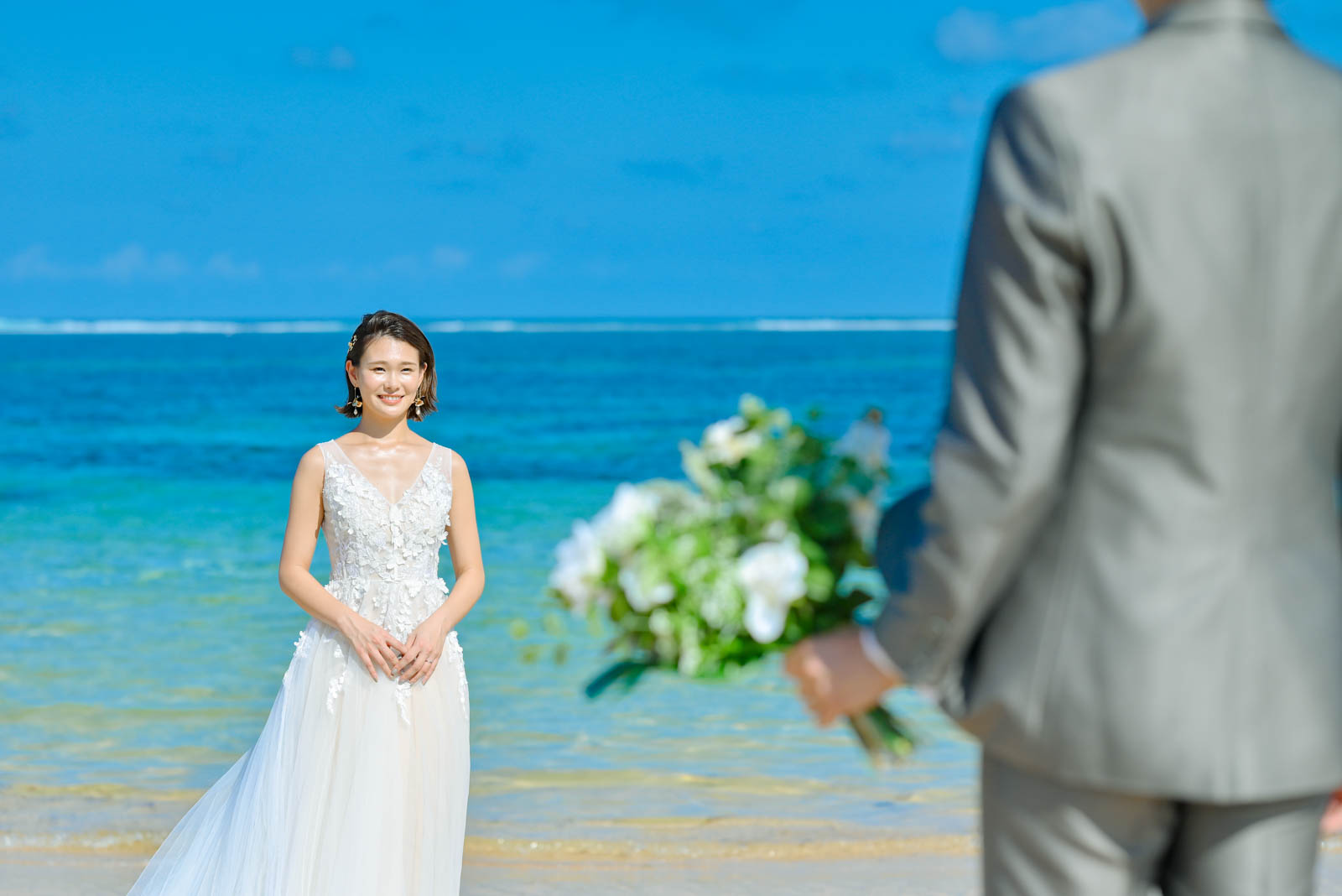 バリ島の海を背景に、新婦の前でブーケを持つ新郎のビーチフォト。新婦の笑顔が美しい正面ショット