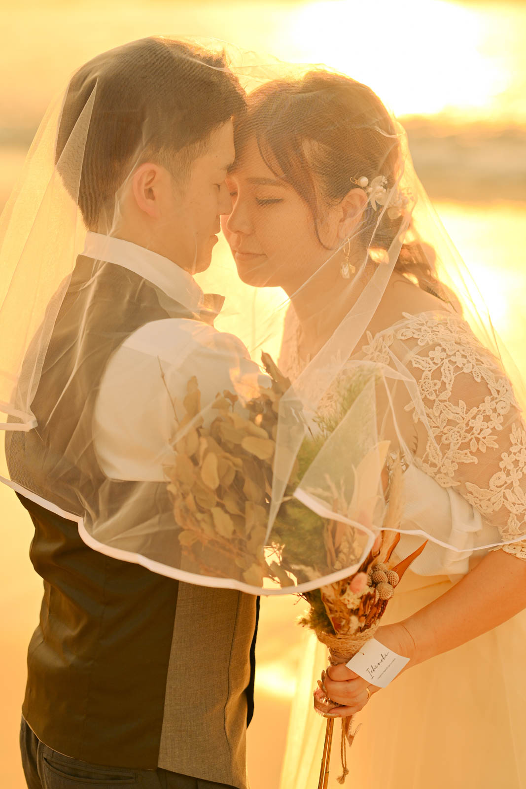 ベール越しに寄り添う新郎新婦の幻想的なサンセットフォト